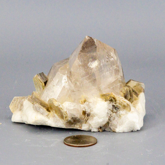 Crystal rock with a penny for scale on a gray background