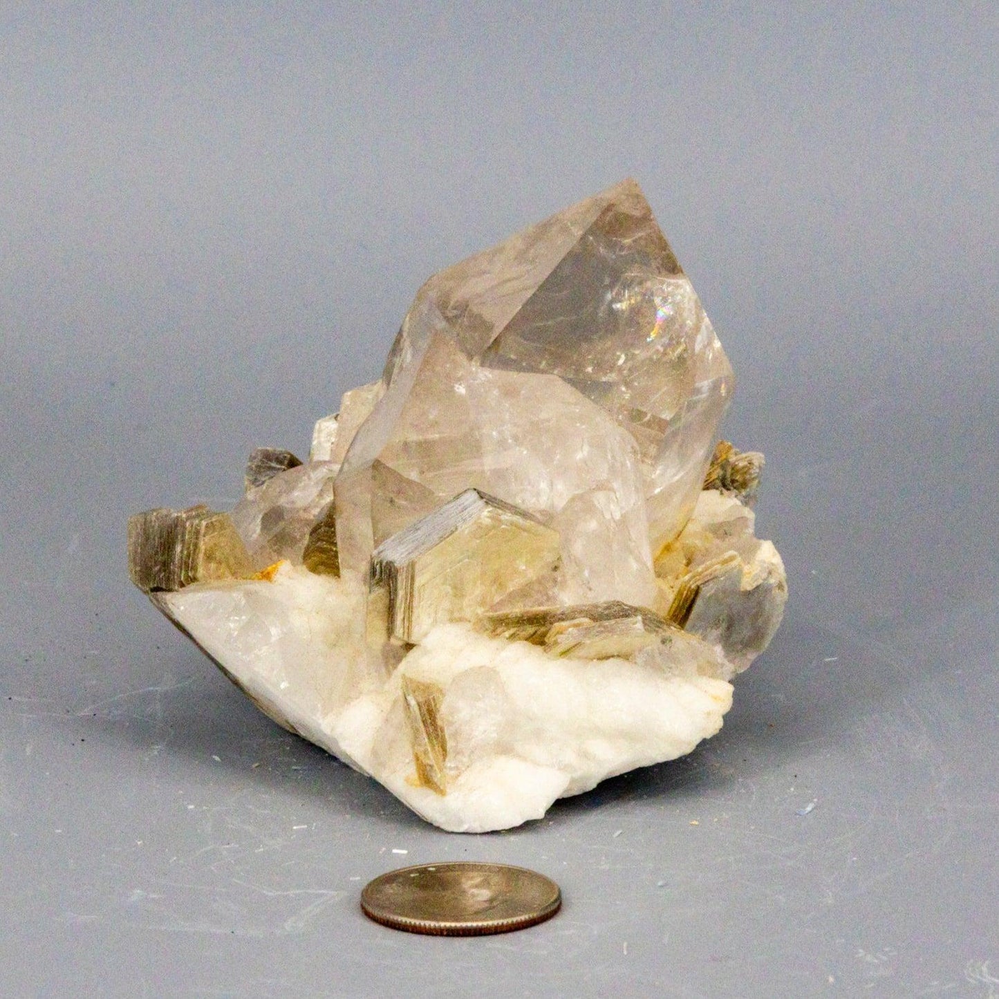 Clear quartz Crystal rock cluster with a penny for scale on a gray background