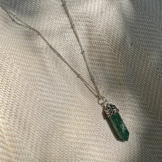 Necklace with a green crystal pendant on a textured beige surface