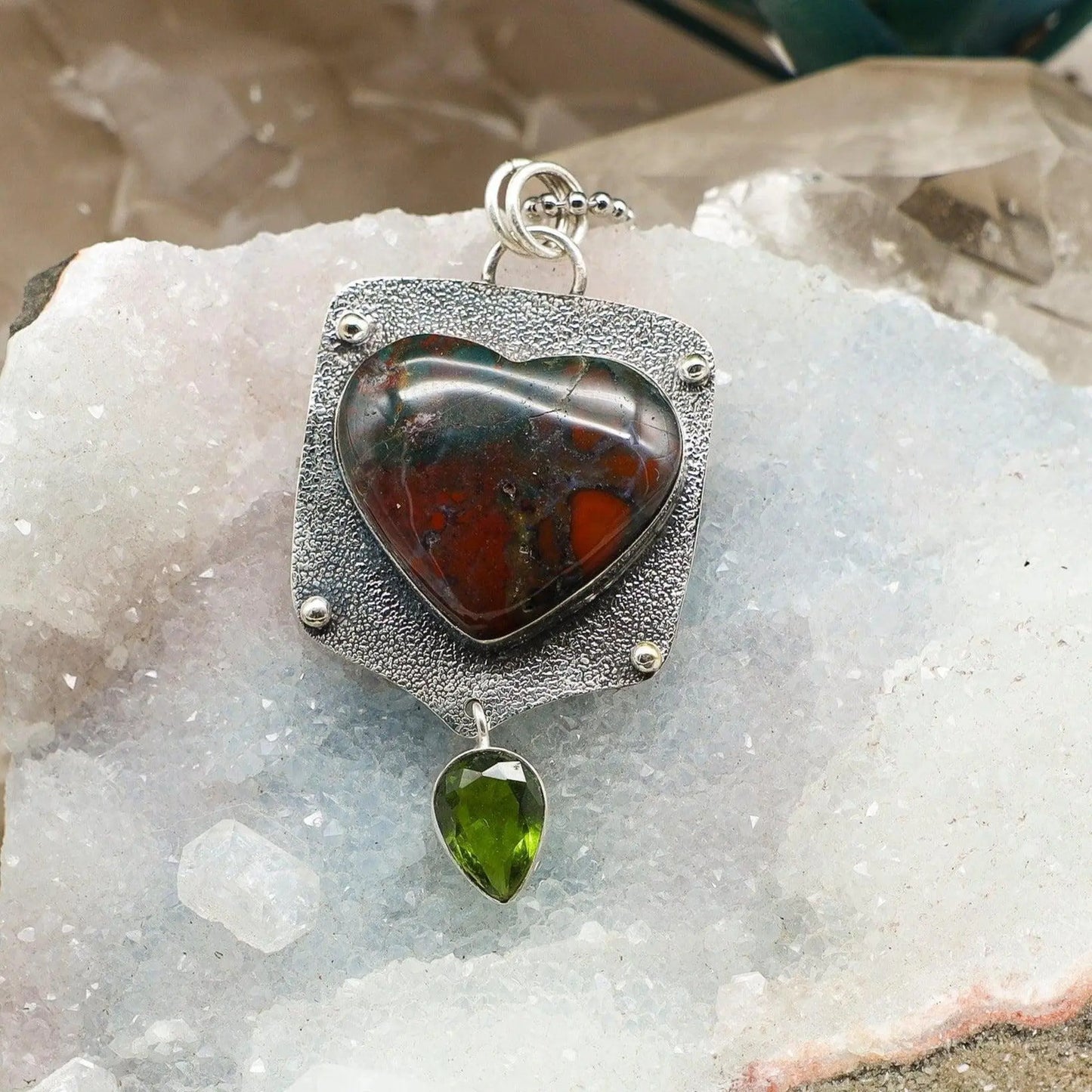 Heart-shaped bloodstone pendant with a green stone on a crystal surface