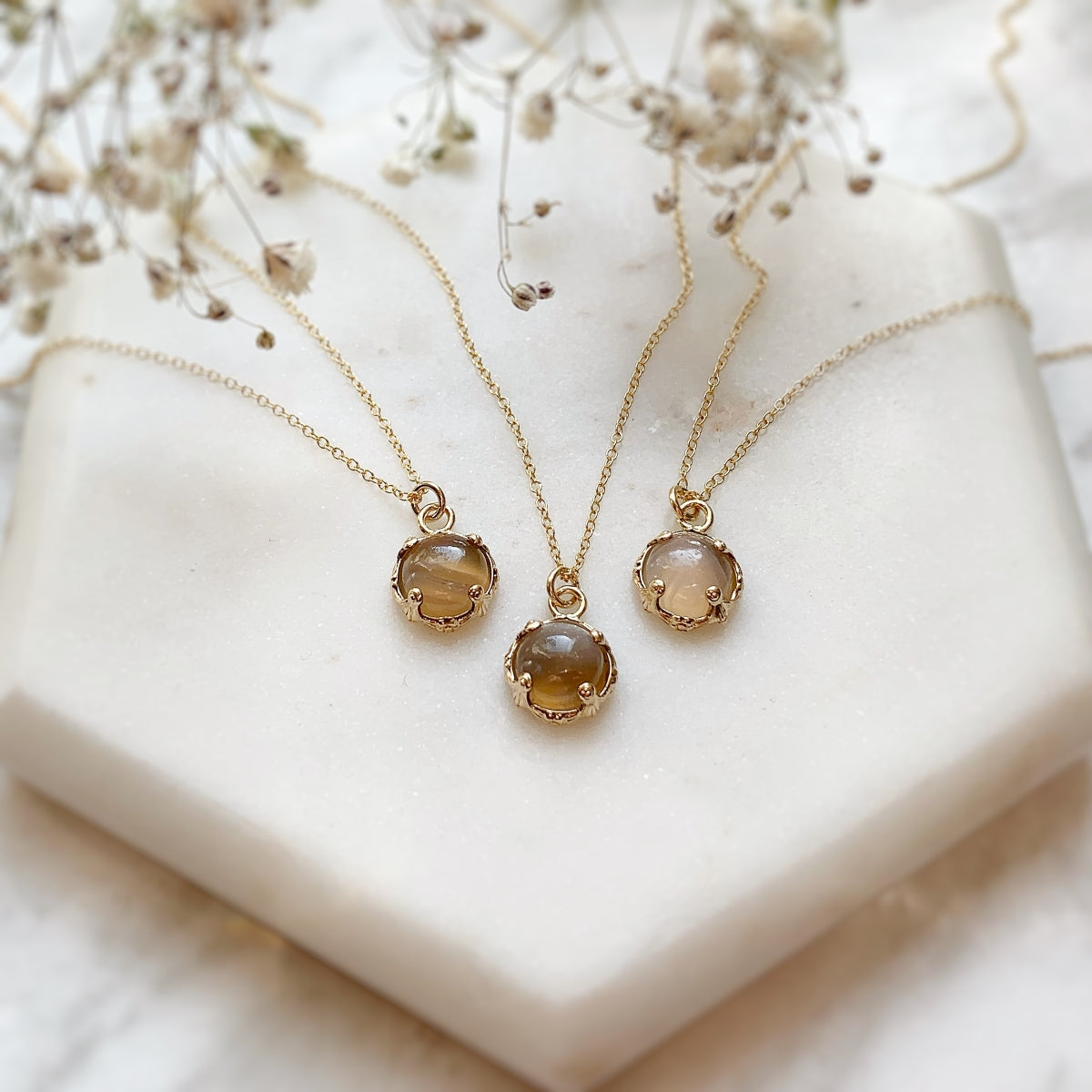 Three gold necklaces with round agate pendants on a white stone surface