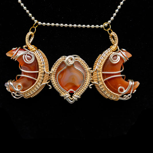 Carnelian agate 3 stone moon phase pendant with gold and silver wire wrapping on a black background