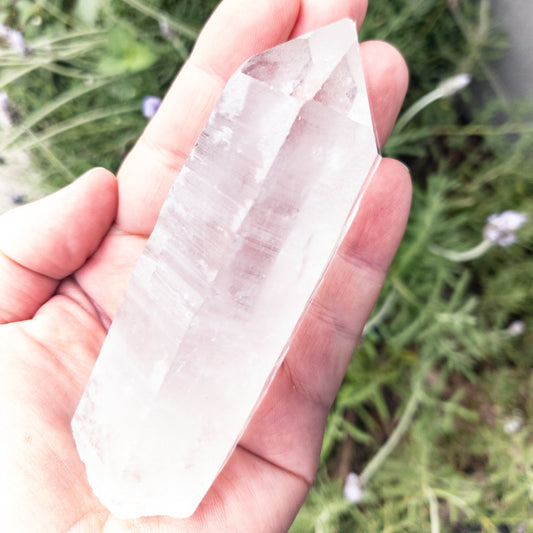 Clear crystal held in a hand with a natural background