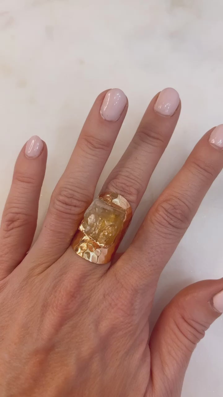 Hand wearing a large yellow gemstone ring on a white background
