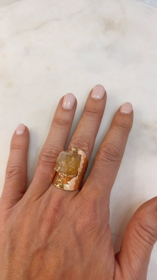 Hand wearing a gold ring with a large gemstone on a marble surface