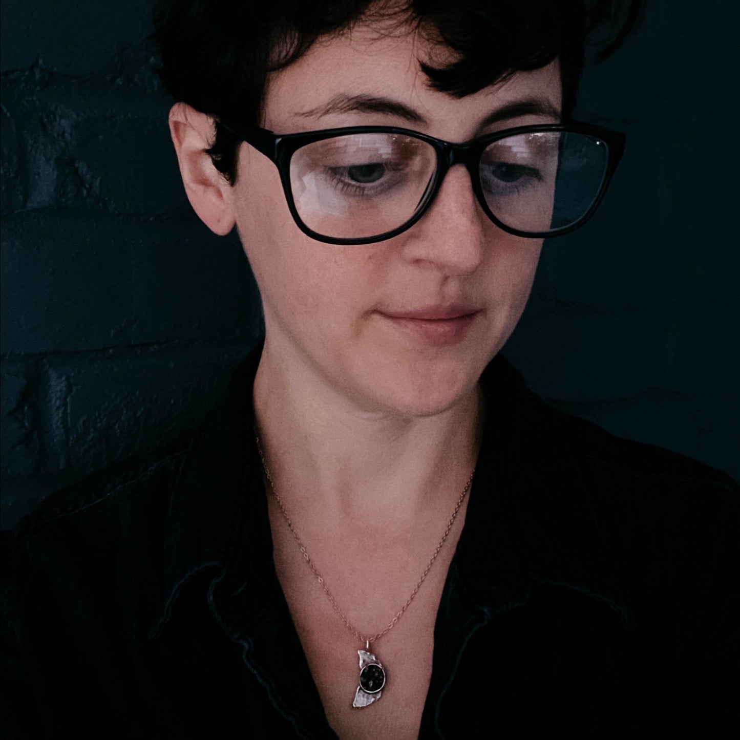 Person wearing glasses wearing a meteorite pendant necklace with a dark background