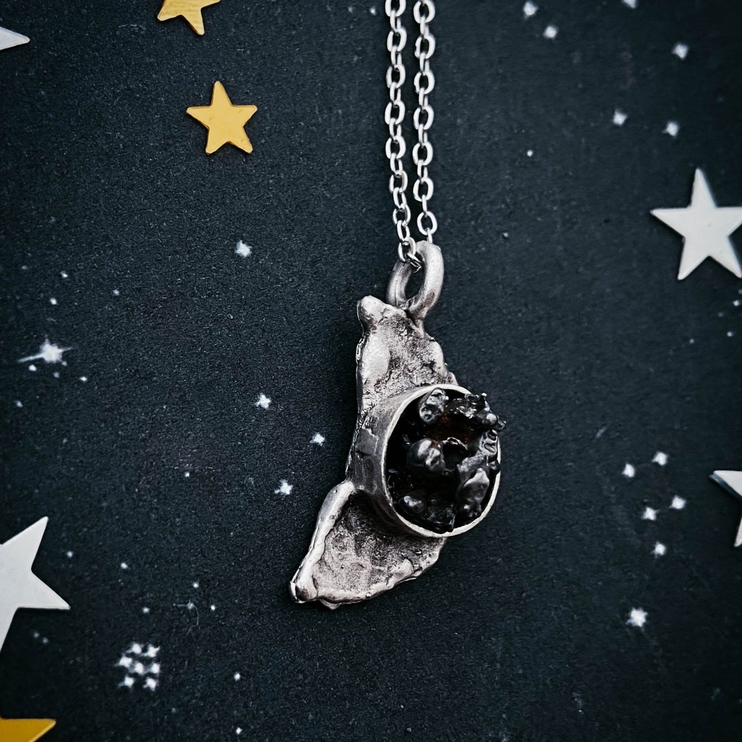 Silver necklace with a unique meteorite pendant on a dark background with star decorations