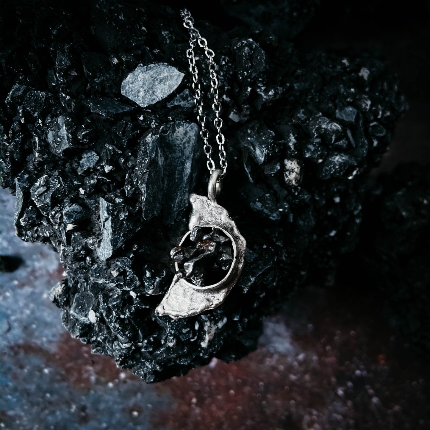 Silver necklace with a meteorite pendant on a dark textured surface