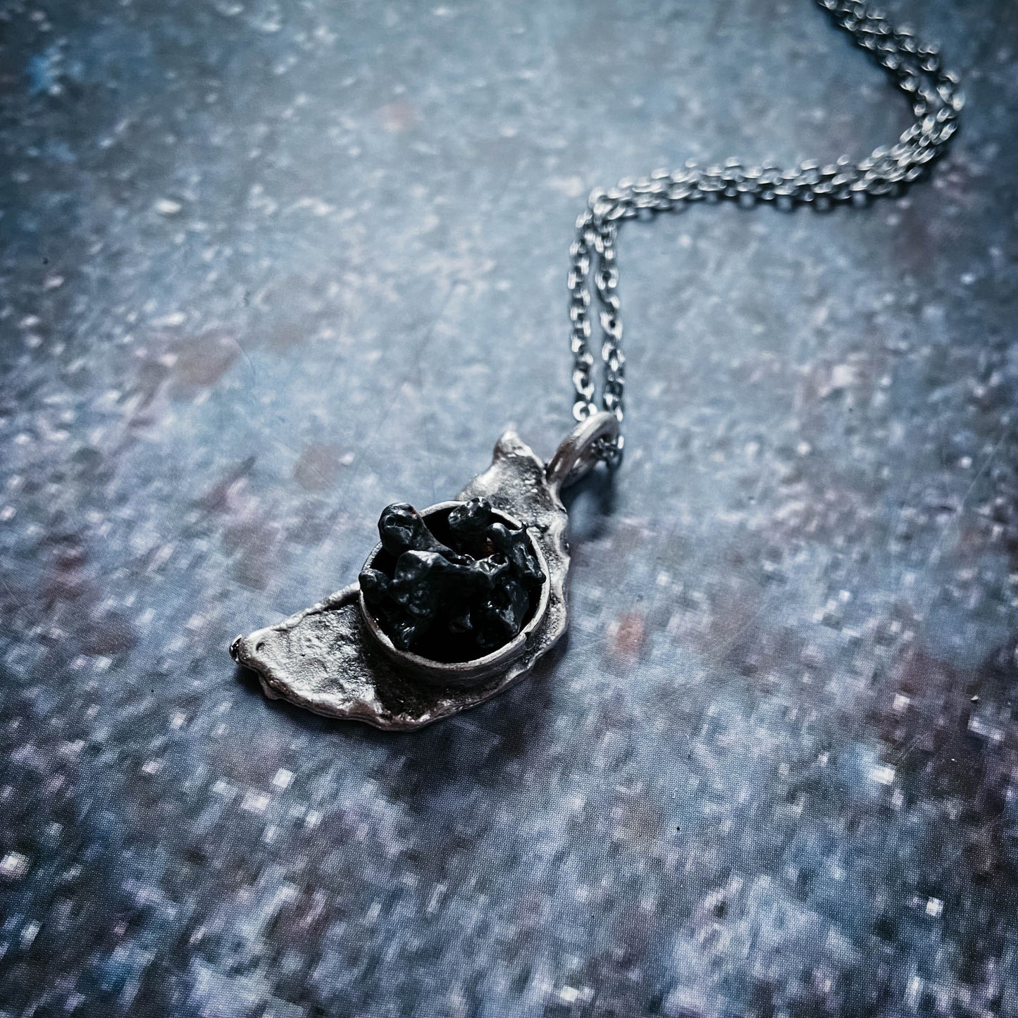 Silver pendant with a meteorite on a textured blue surface