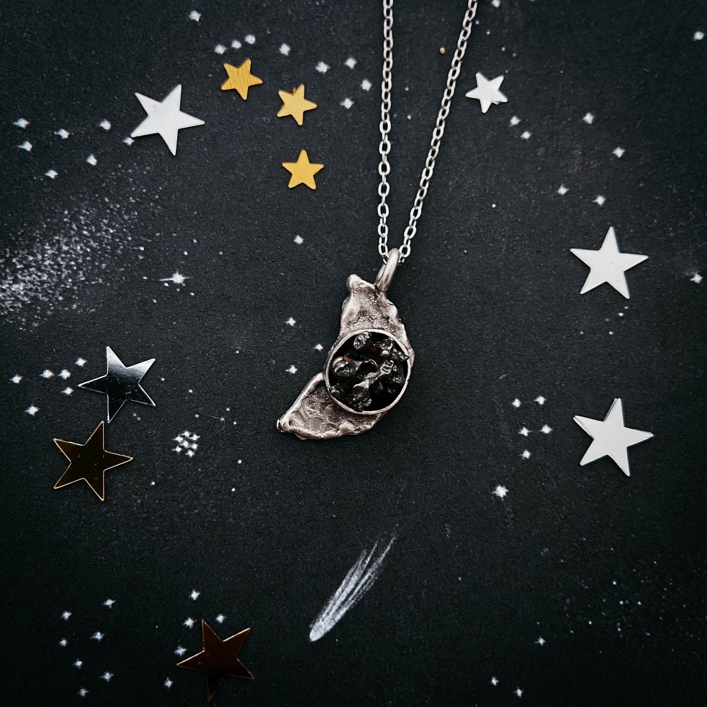 Necklace with a moon pendant with meteorite on a dark background with star decorations