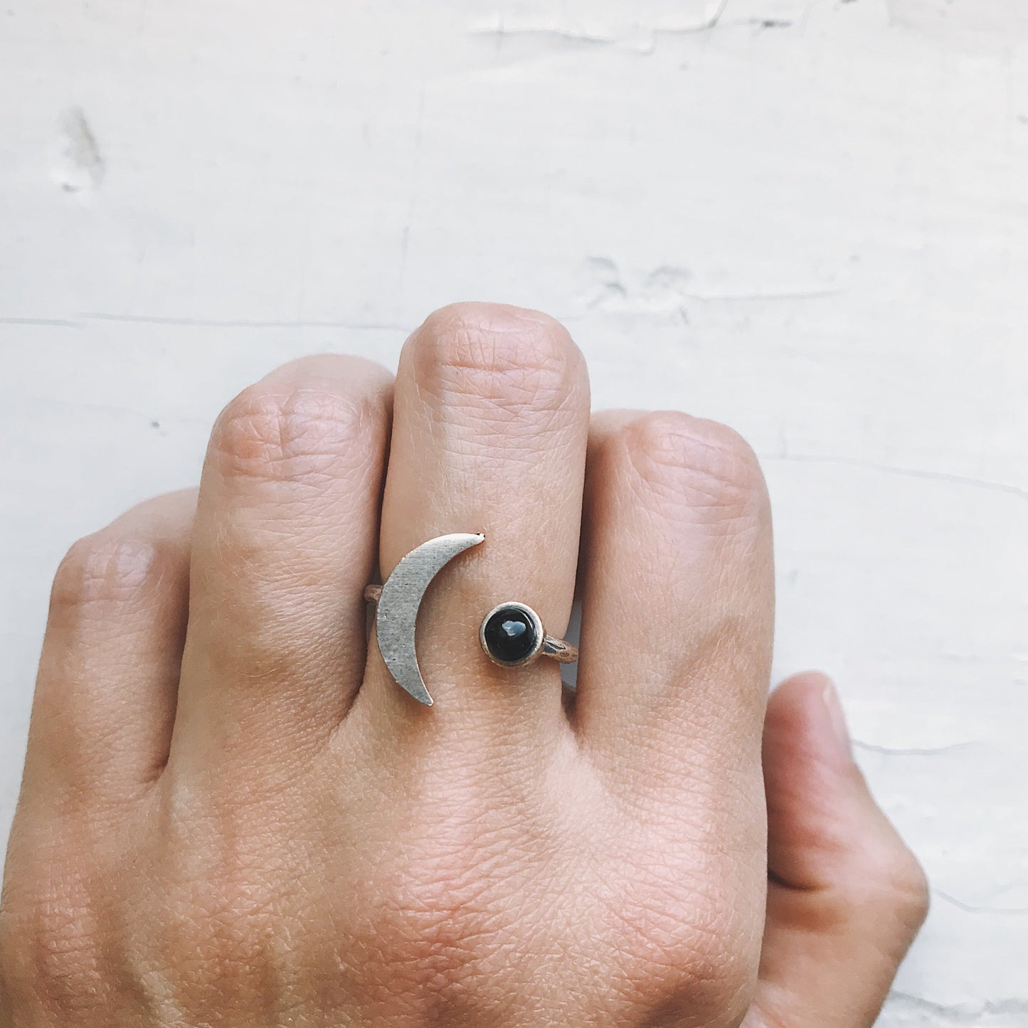 Hand wearing a silver ring with a black onyx gemstone on a light background