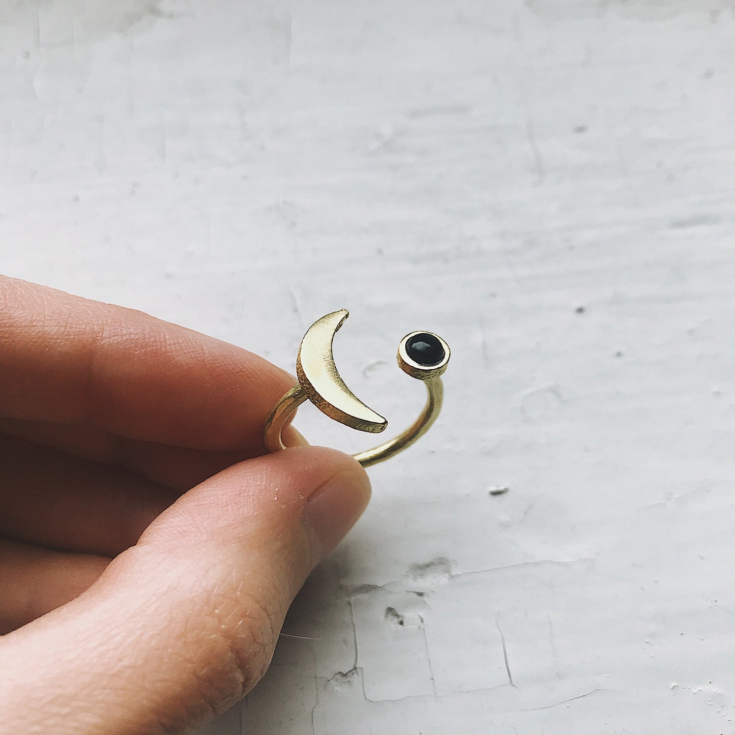 Gold ring with a black onyx gemstone held by a hand on a light gray background