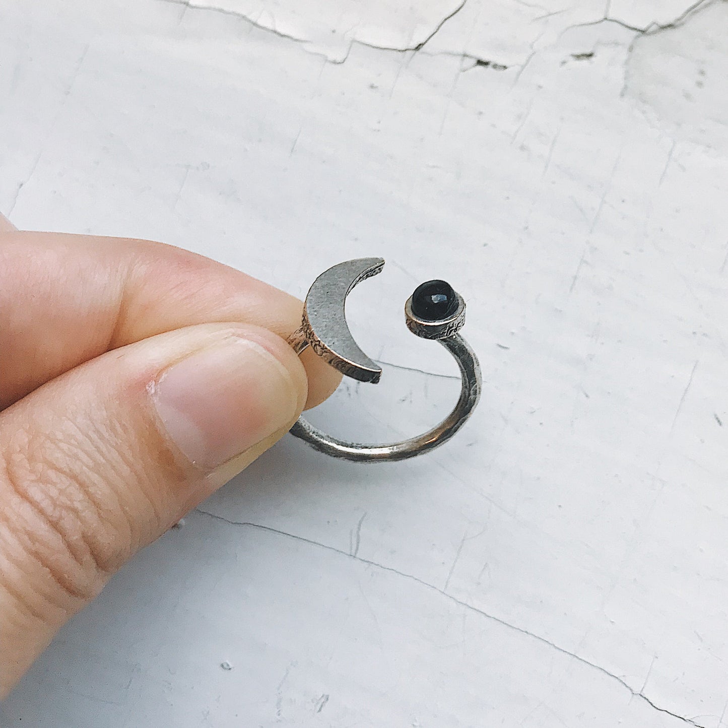Silver ring with a black onyx gemstone held between fingers on a textured white background