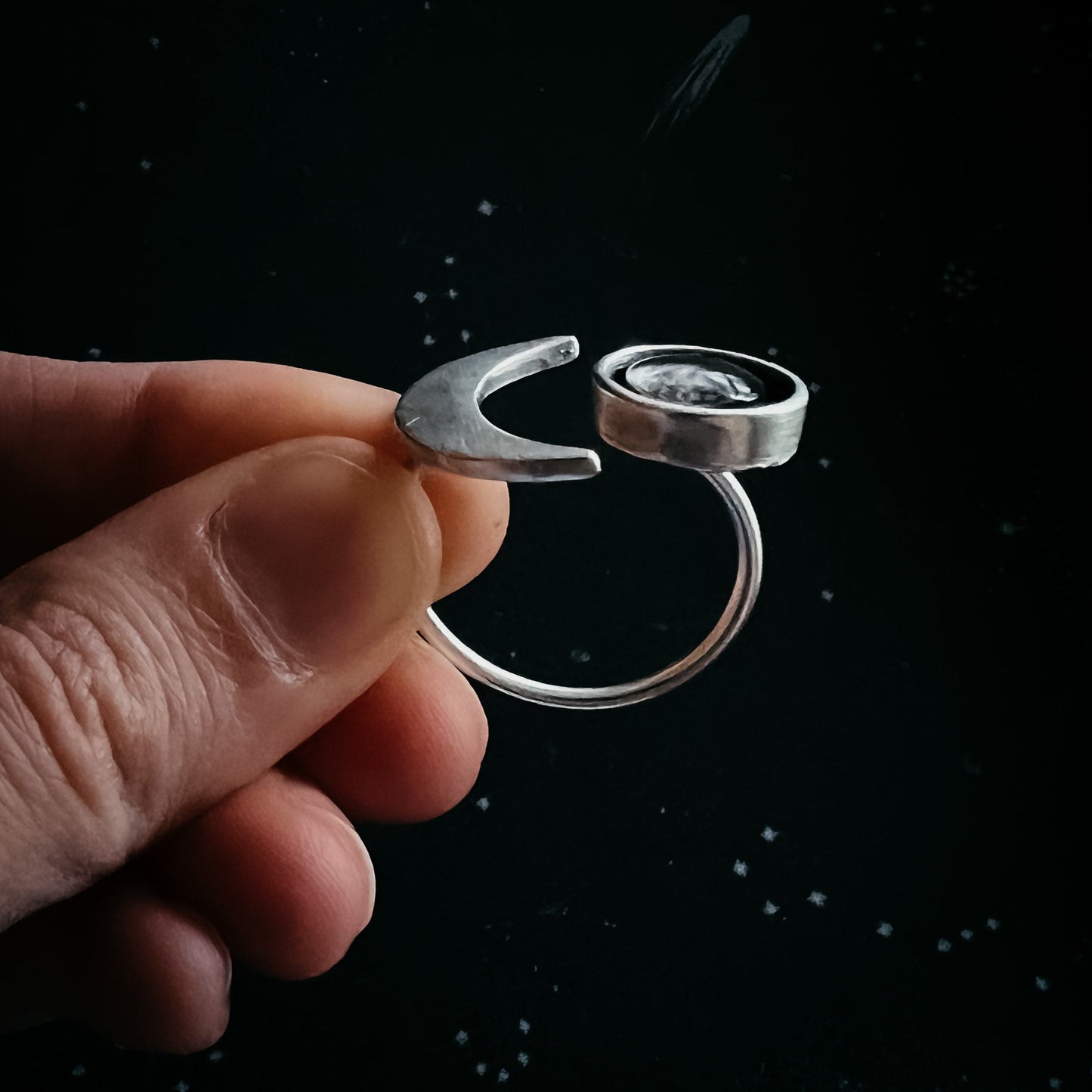 Silver ring with a stone held by a hand against a black background