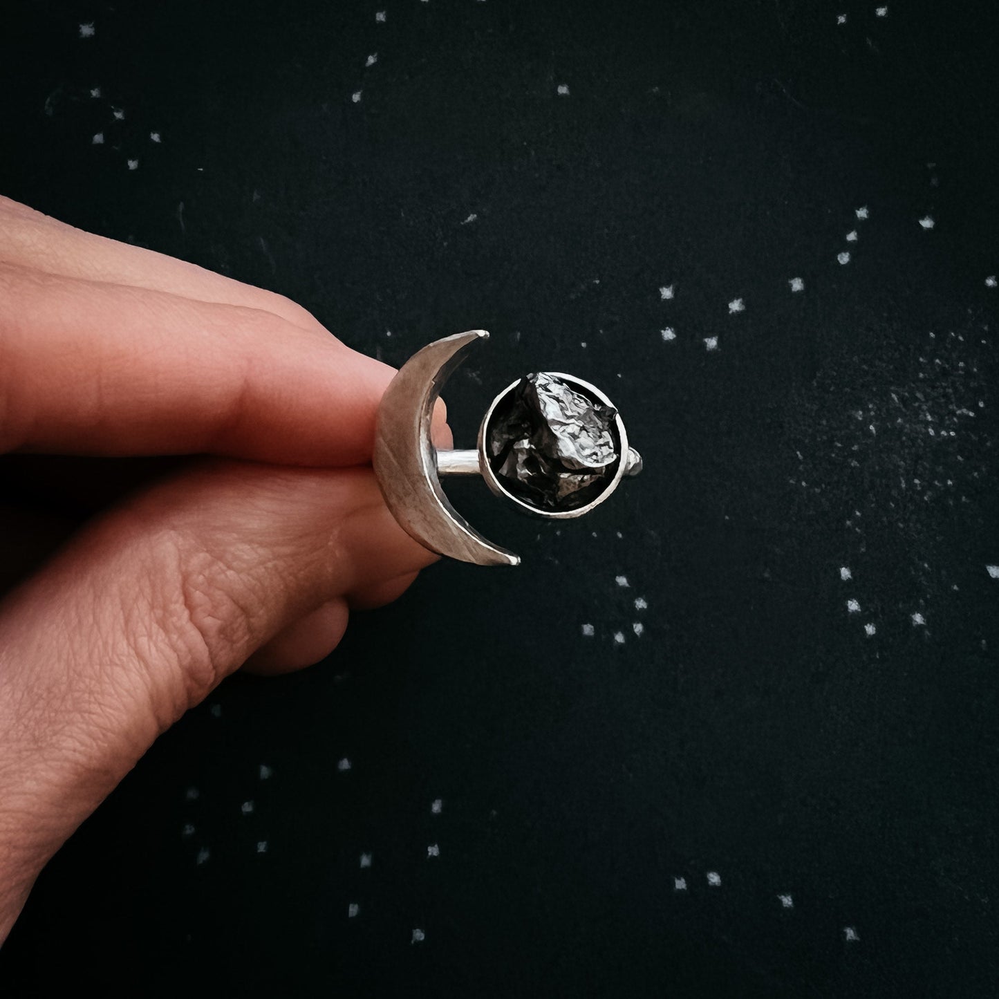 Silver ring with authentic meteorite held by a hand against a black background
