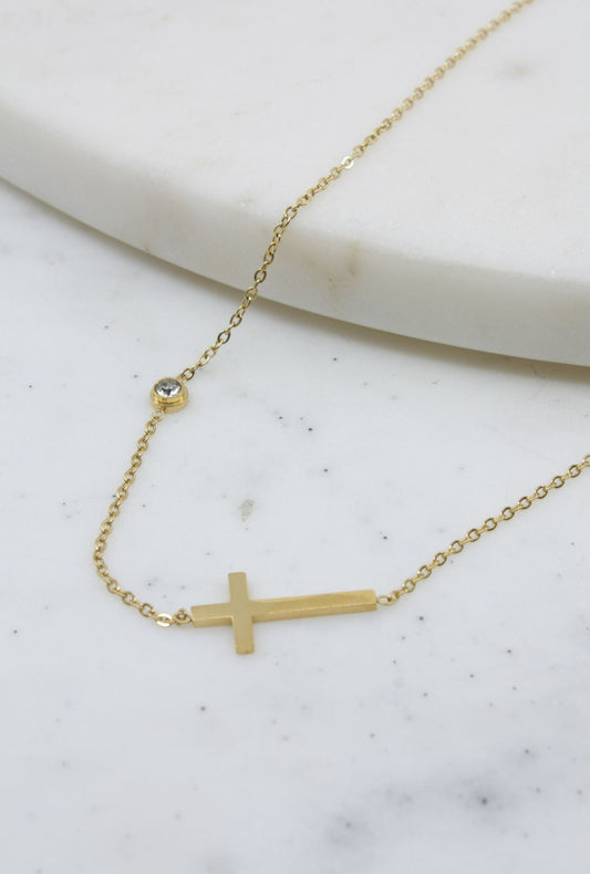 Gold necklace with a small cross pendant on a marble surface