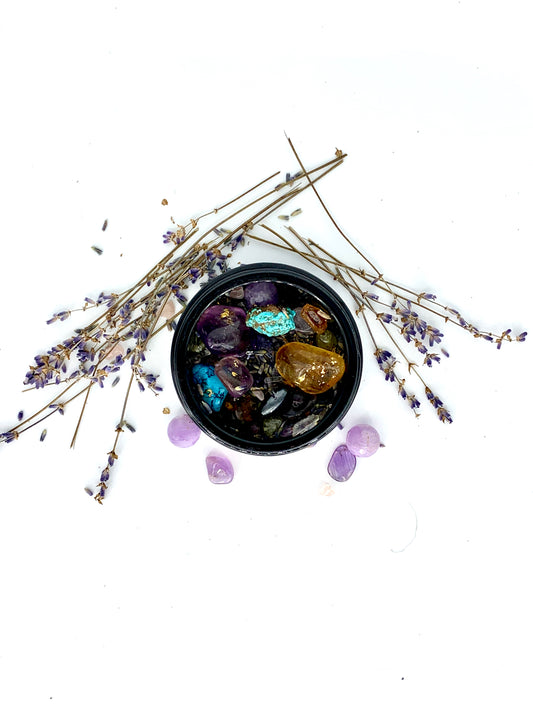 Black bowl with colorful crystals surrounded by lavender flowers on a white background