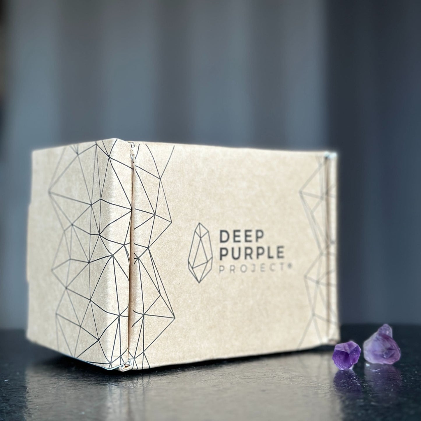 Beige box with geometric design and 'Deep Purple Project' branding on a dark surface with purple crystals.