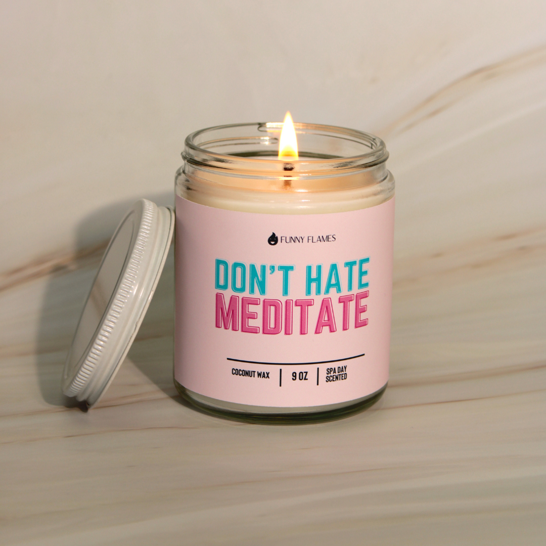 Candle in a jar with a pink label reading 'Don't Hate Meditate' on a wooden surface.
