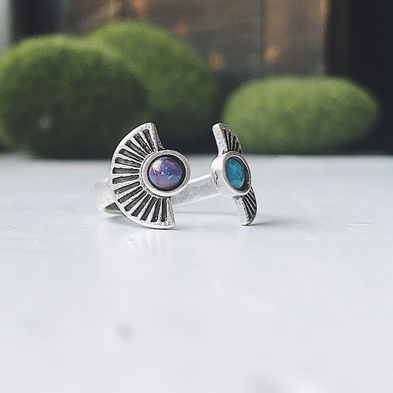 Silver rings with embedded stones on a white surface with greenery in the background