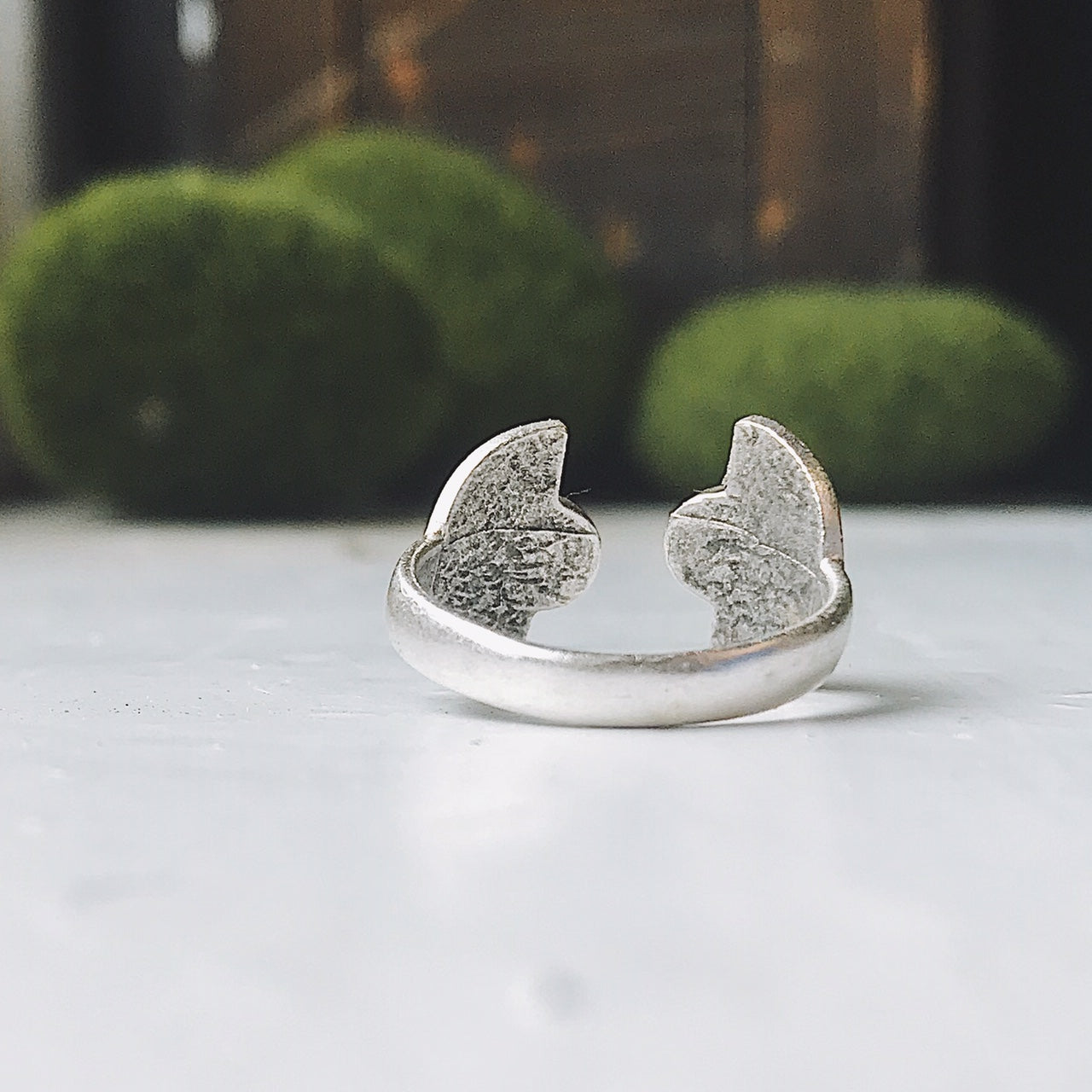 Silver ring on a white surface with a blurred green background