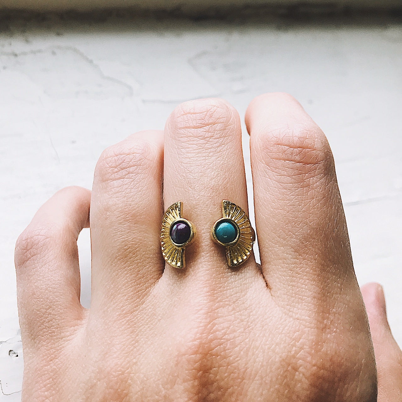 Gold ring with gemstones on a hand against a neutral background