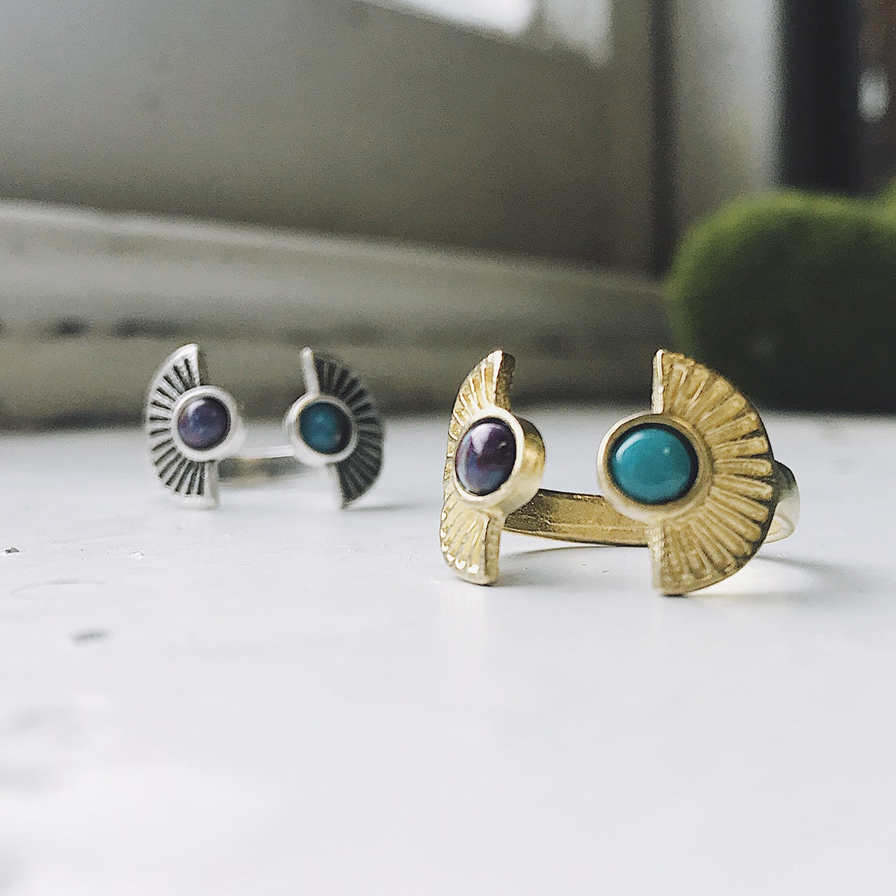 Two rings, one gold and one silver, with gemstones on a white surface.