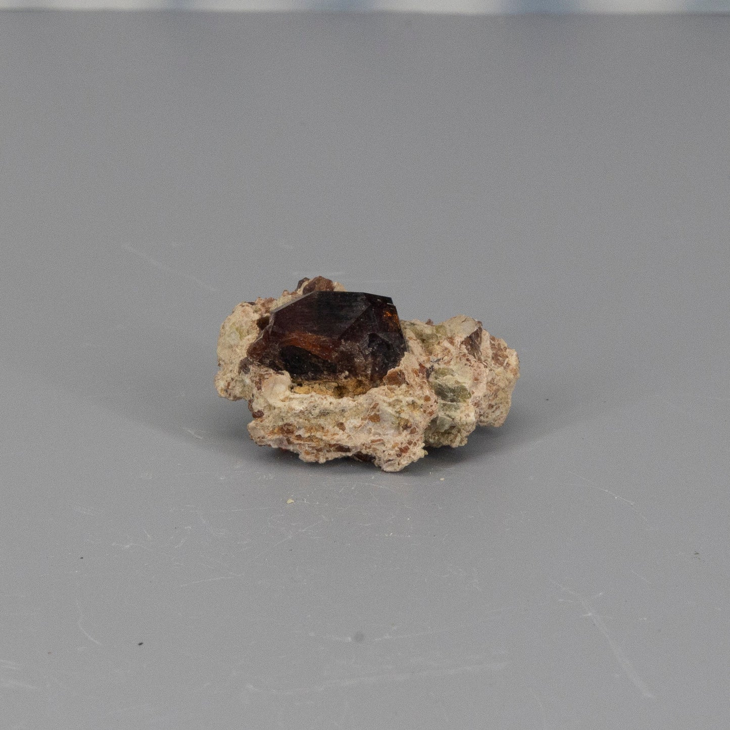 Mineral sample with a garnet crystal on a gray background