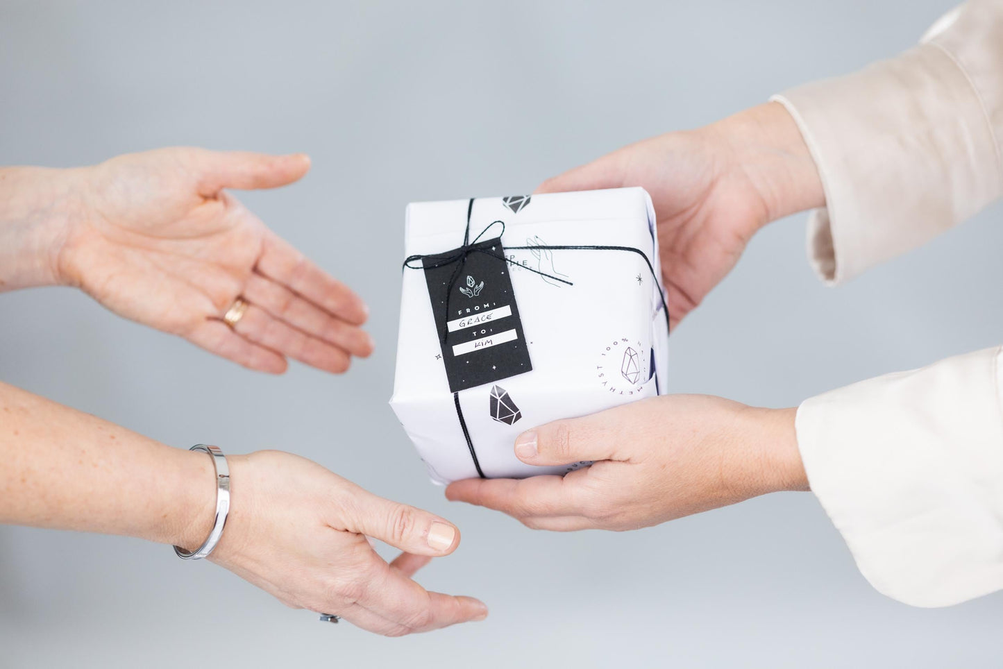Two pairs of hands exchanging a white product packaging with black design on a gray background
