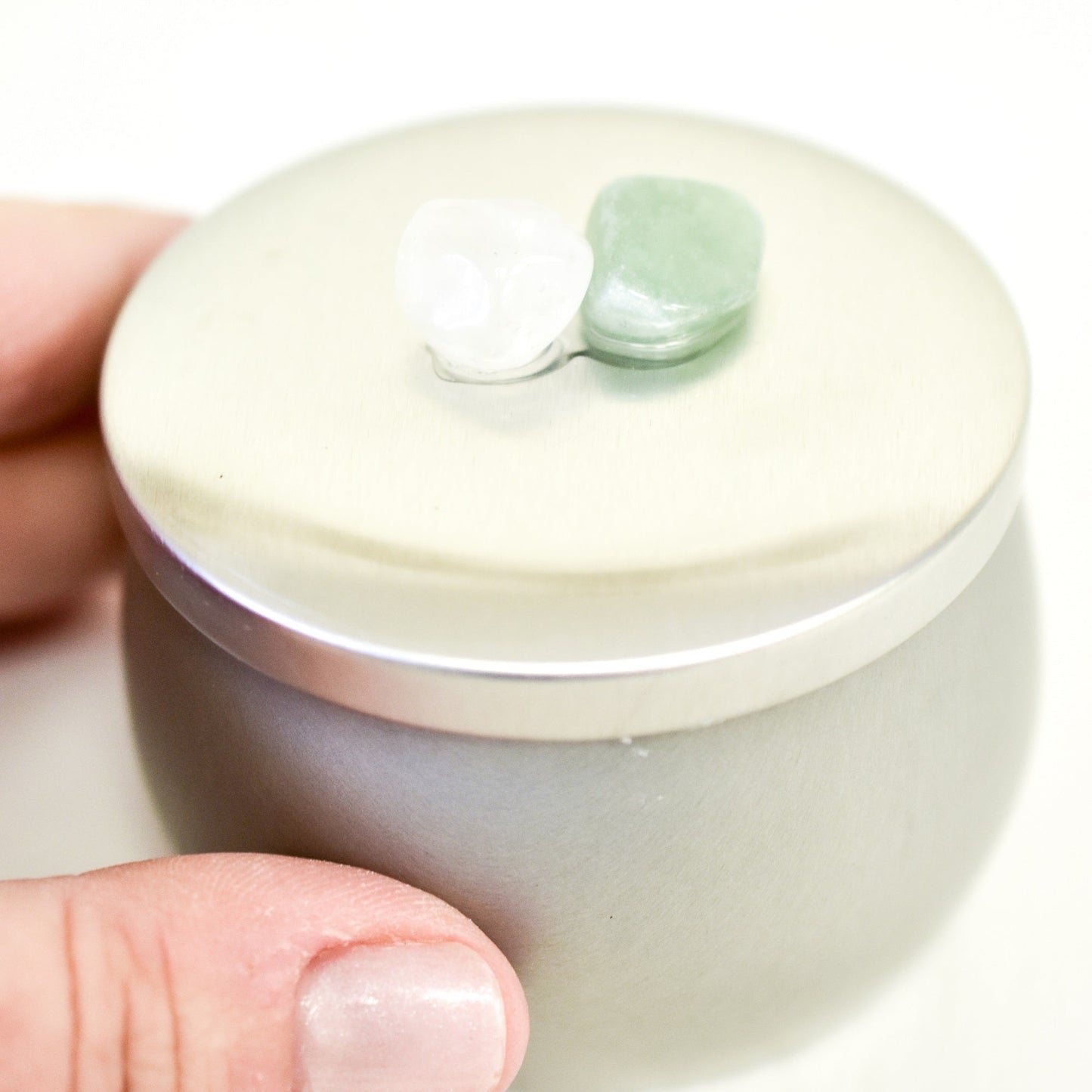 Small ceramic container with a jade lid held by a hand on a white background