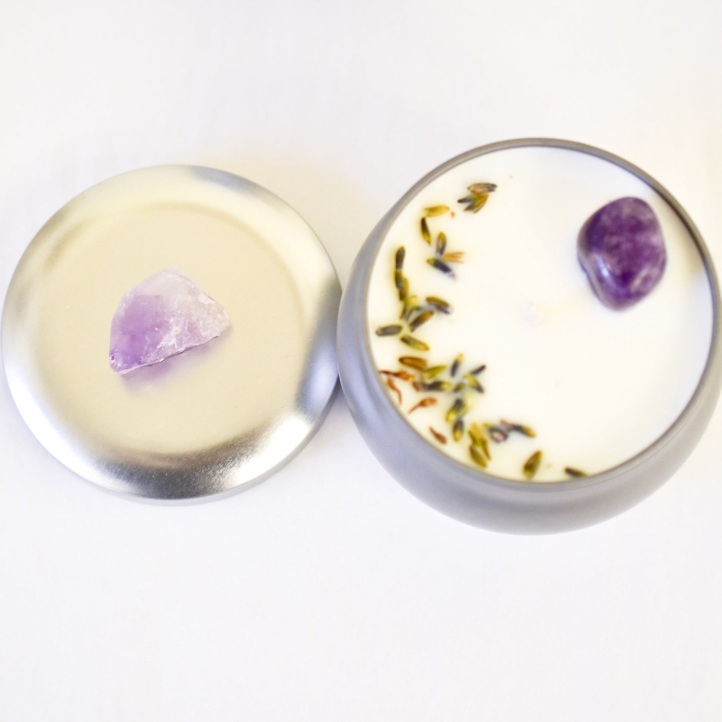 Round container candle with a purple crystal and dried herbs on a white background