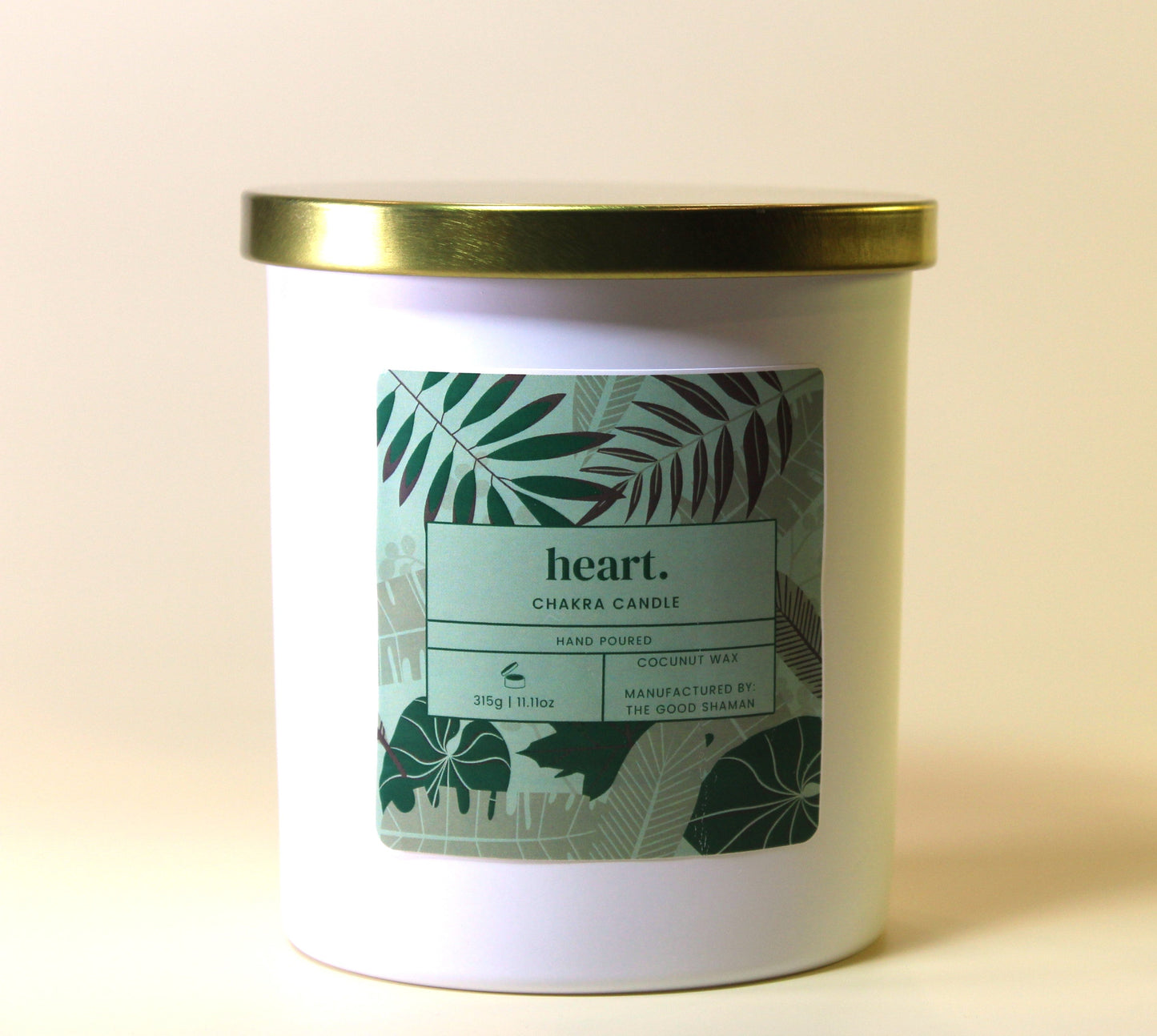 White heart chakra candle with a gold lid and leaf-patterned label on a light background