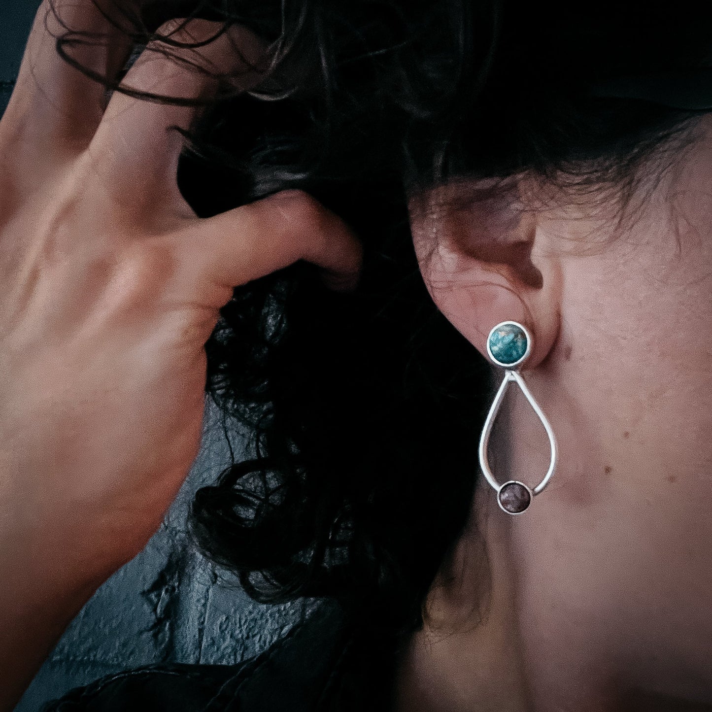 Close-up of an earring being worn, with a hand adjusting hair.
