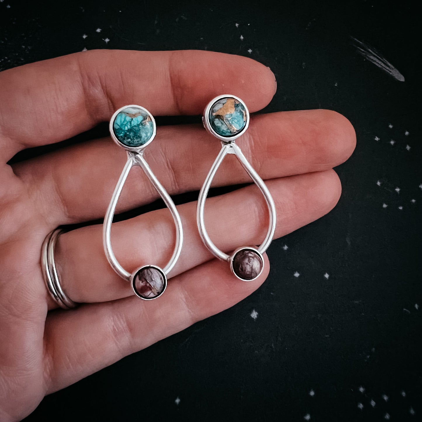 Silver earrings with gemstones held in a hand against a dark background