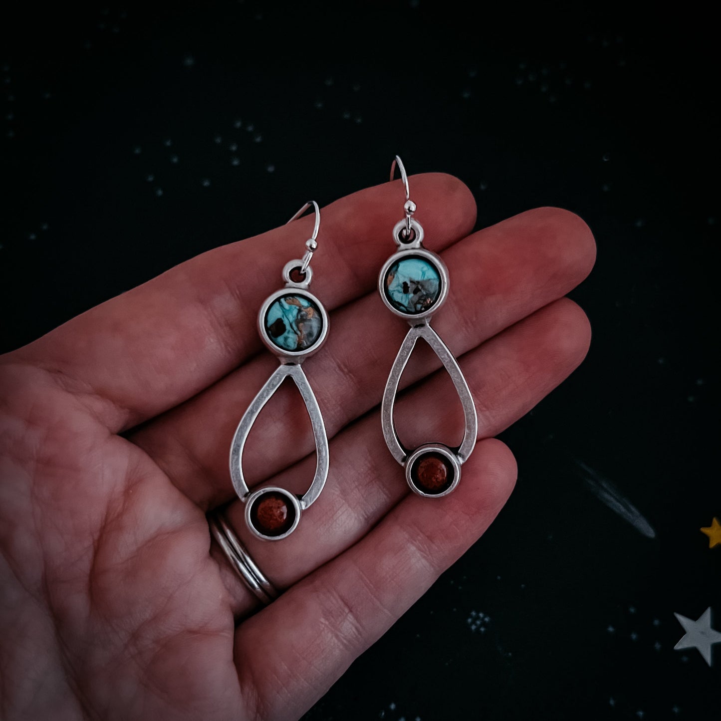 Silver earrings with gemstones held in a hand against a dark background