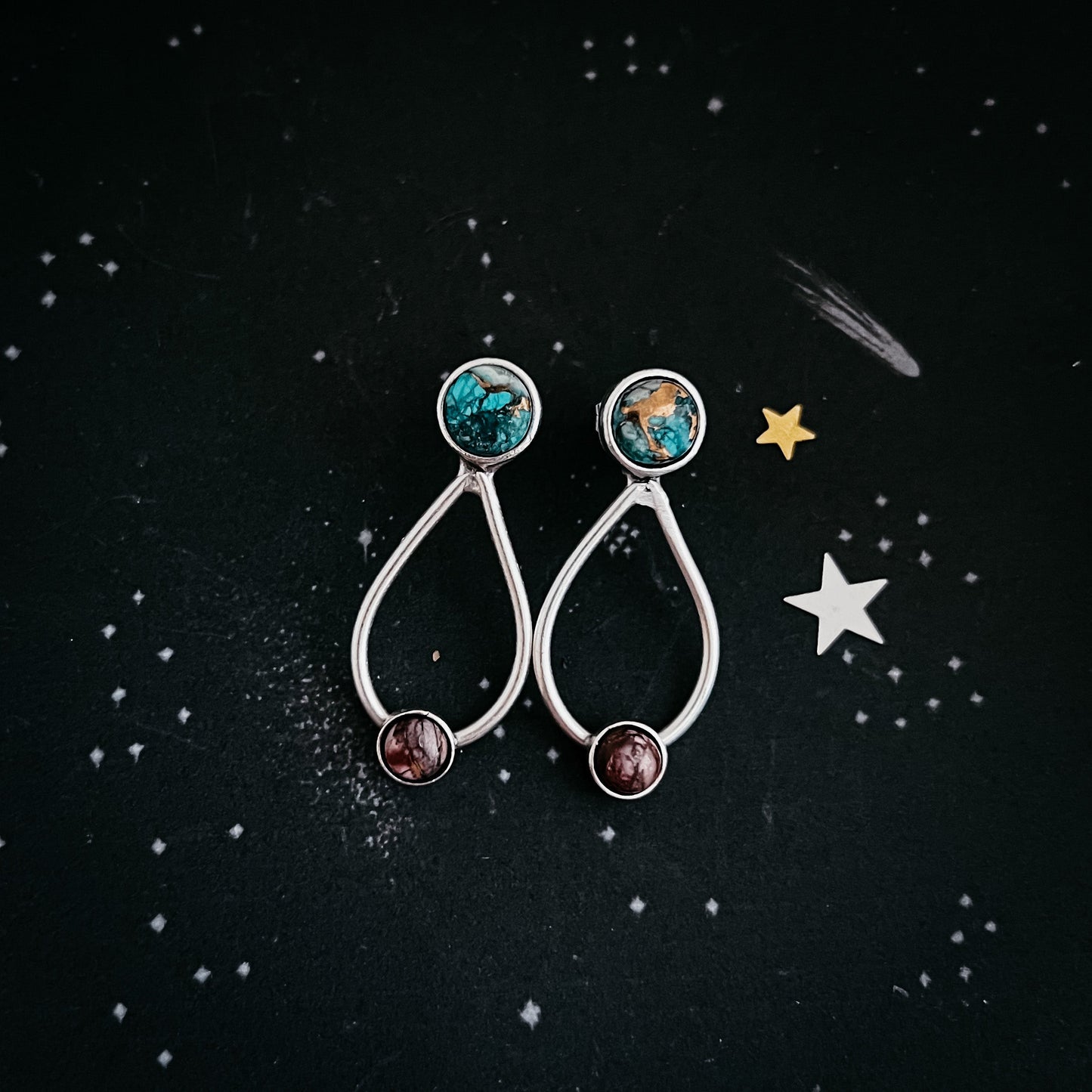 Pair of earrings with gemstones on a black background with star decorations