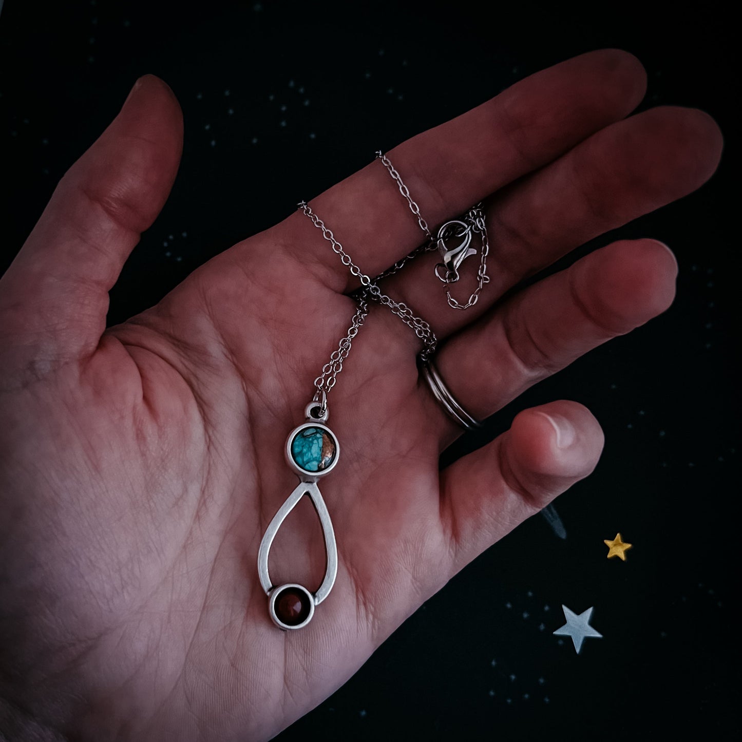 Hand holding a silver necklace with a turquoise pendant against a dark background