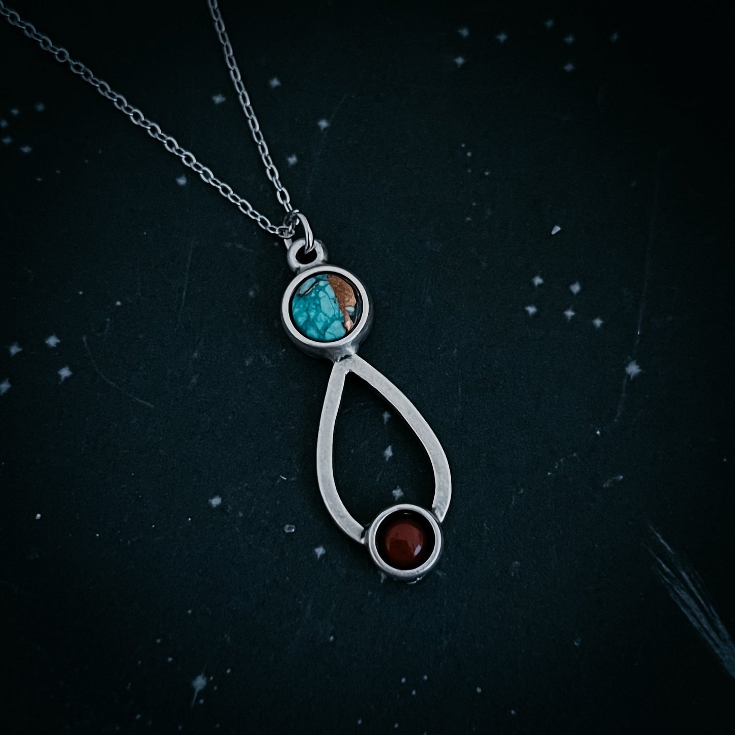 Silver necklace with a pendant featuring turquoise and red stones on a dark background