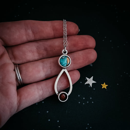 Silver necklace with a pendant held in a hand against a dark background with stars.