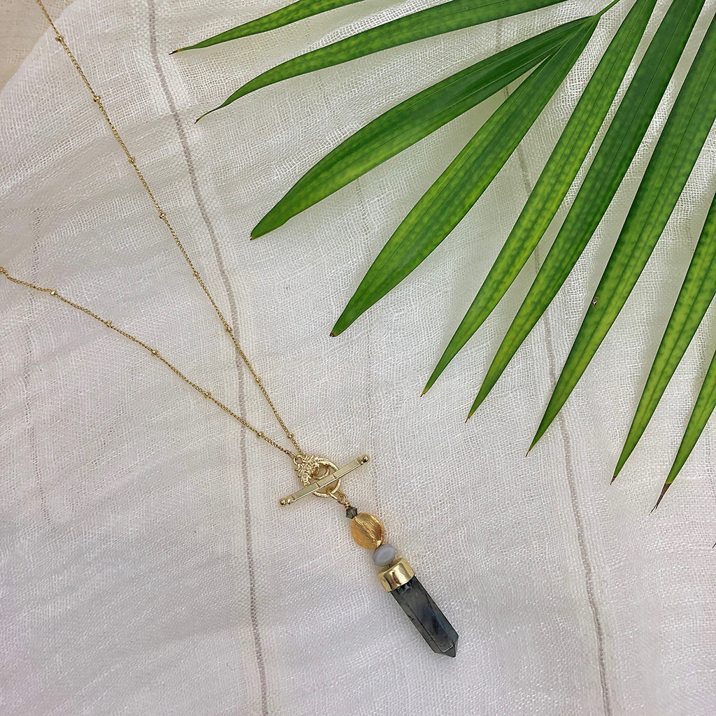 Necklace with a labradorite pendant on a white fabric background with green leaves