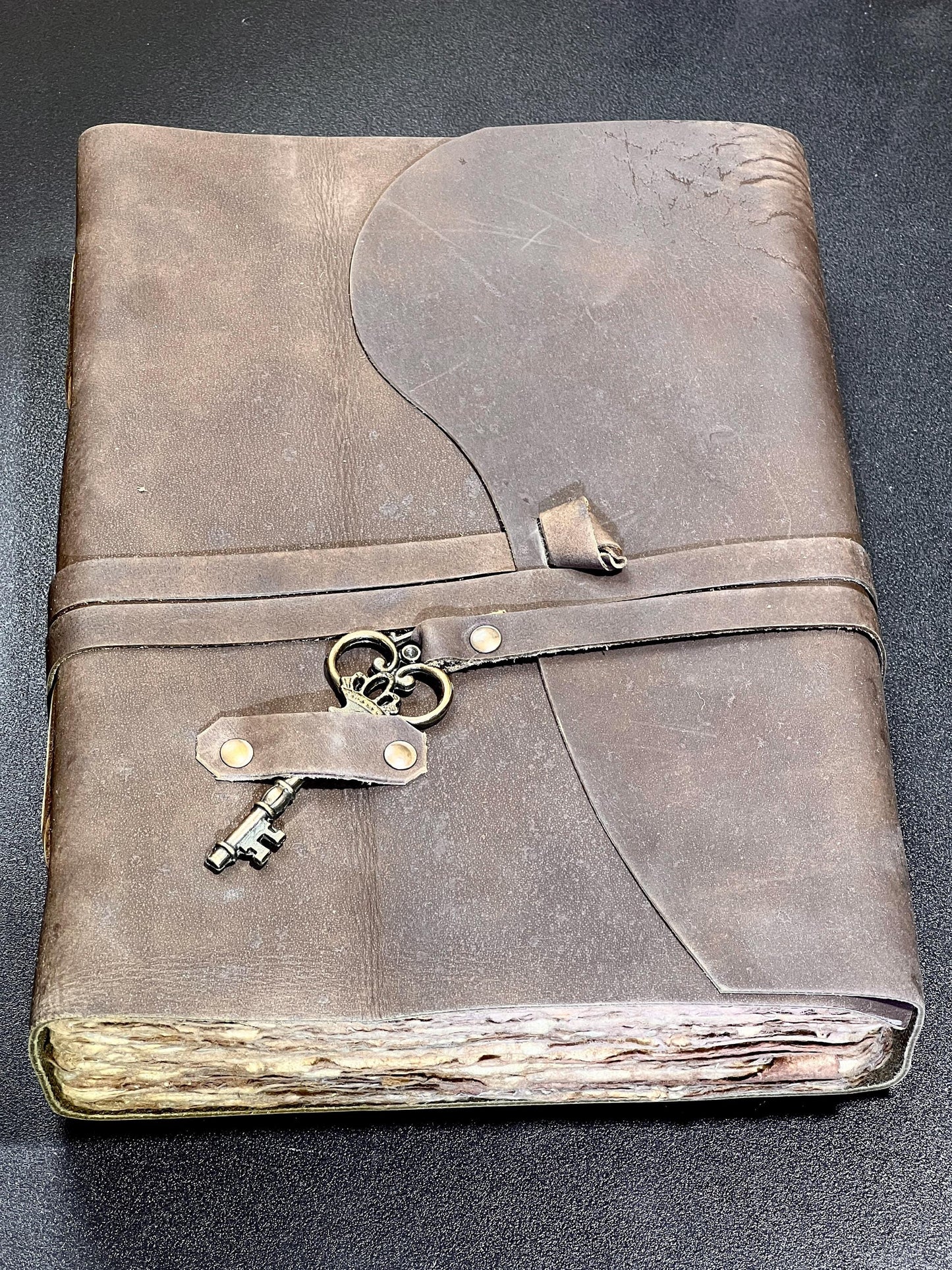 Brown leather-bound book with decorative key locks on a dark background
