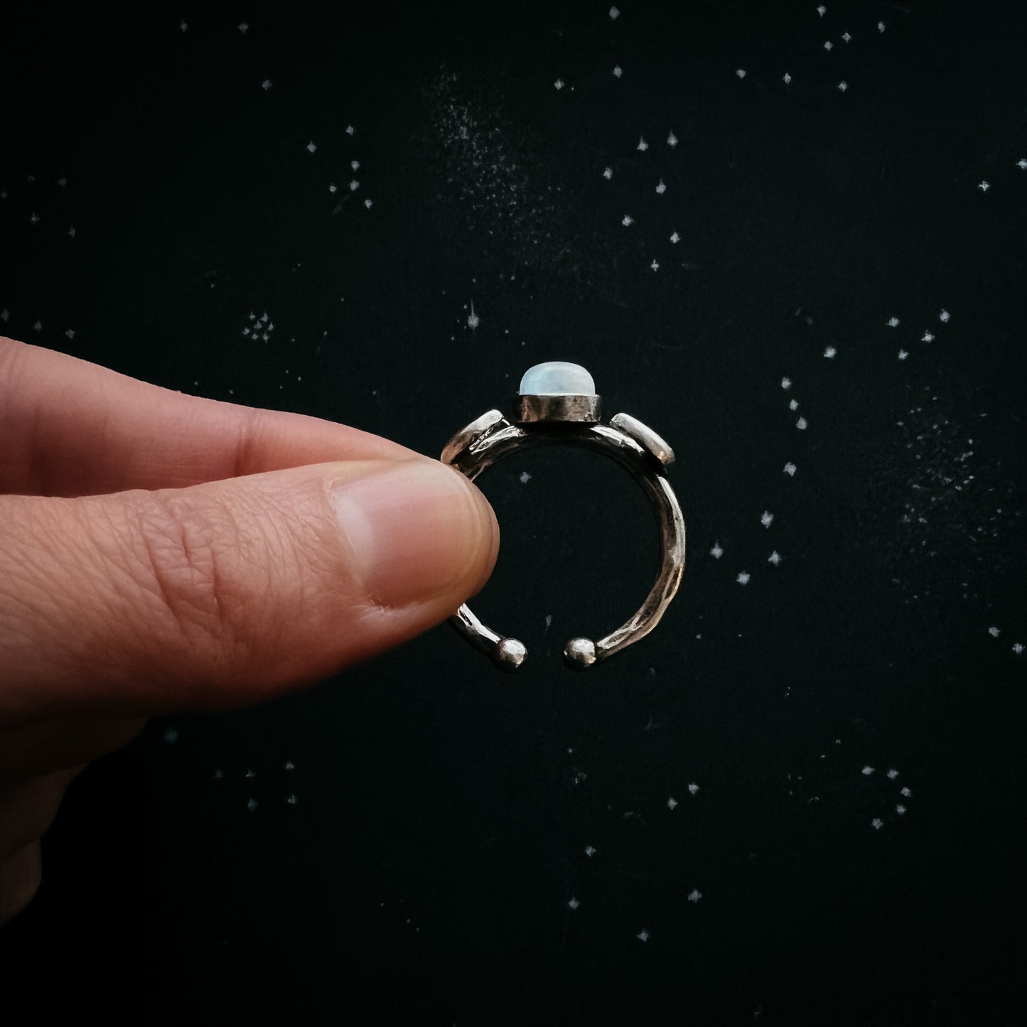 Silver ring with moonstone held between fingers against a dark background