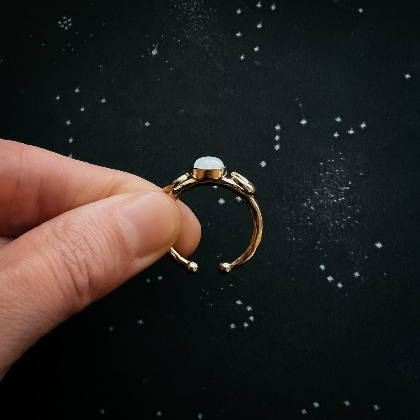 Gold ring with a moonstone gemstone held by a hand against a black background