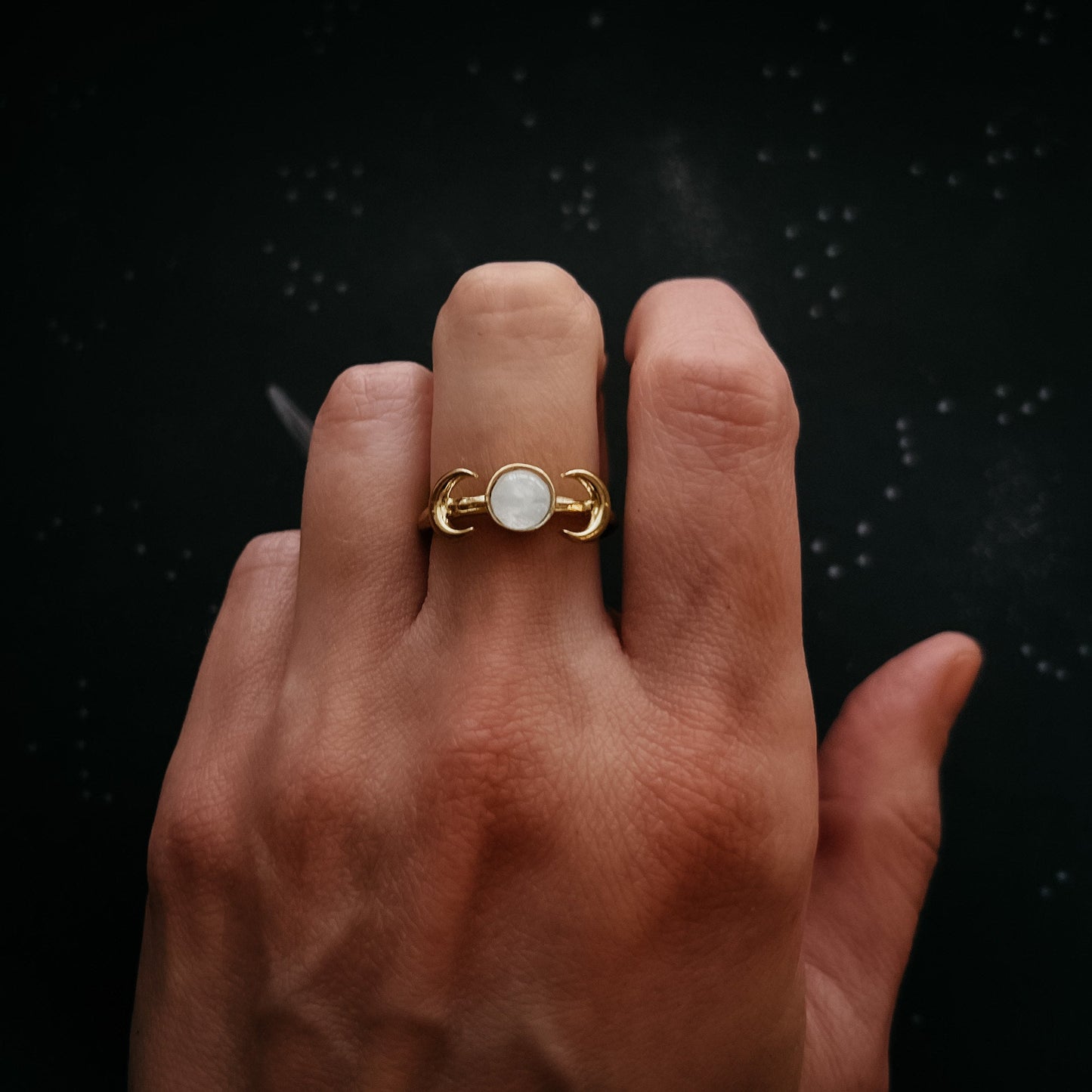Hand wearing a gold ring with a moonstone on a black background