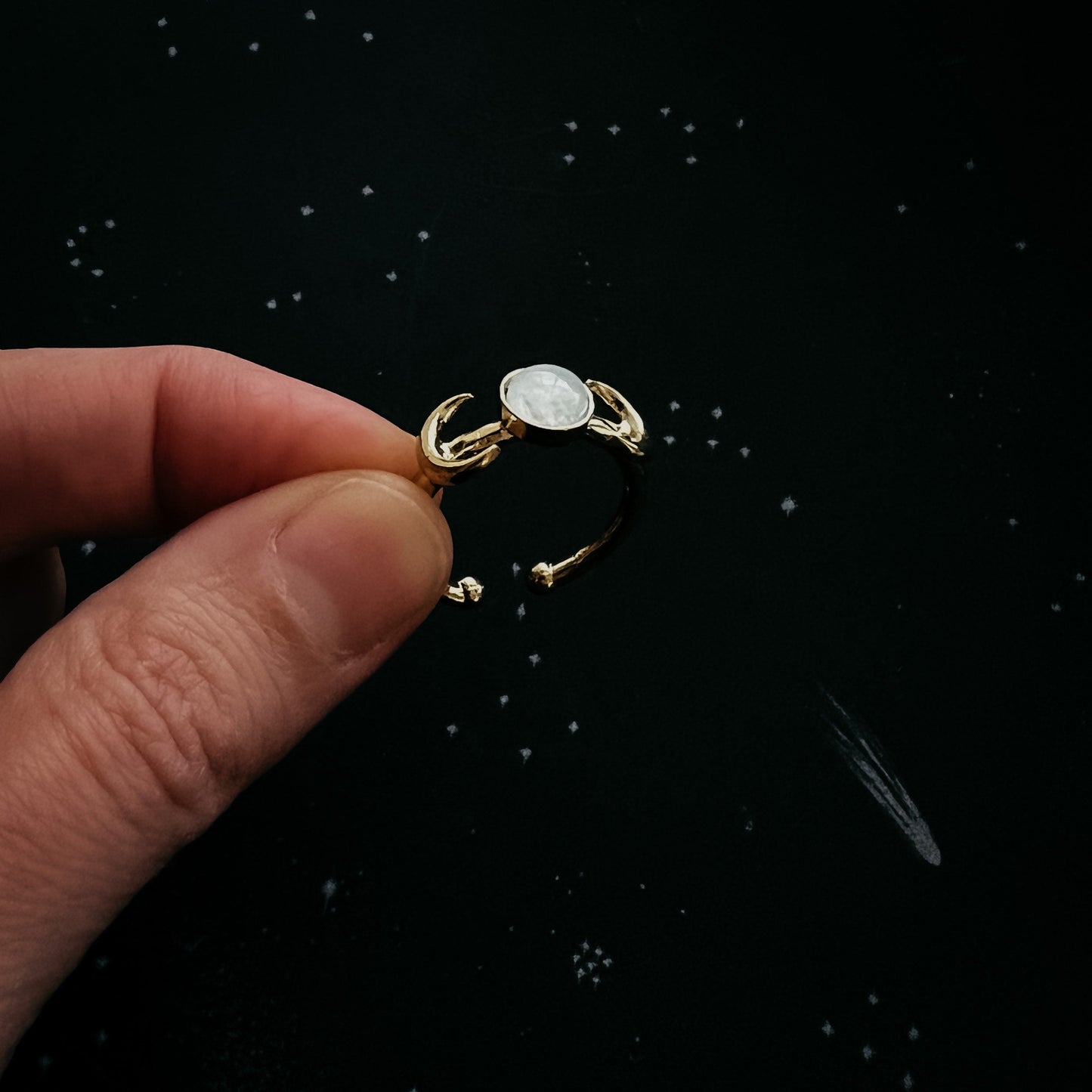 Gold ring with a central gemstone held by a hand against a black background