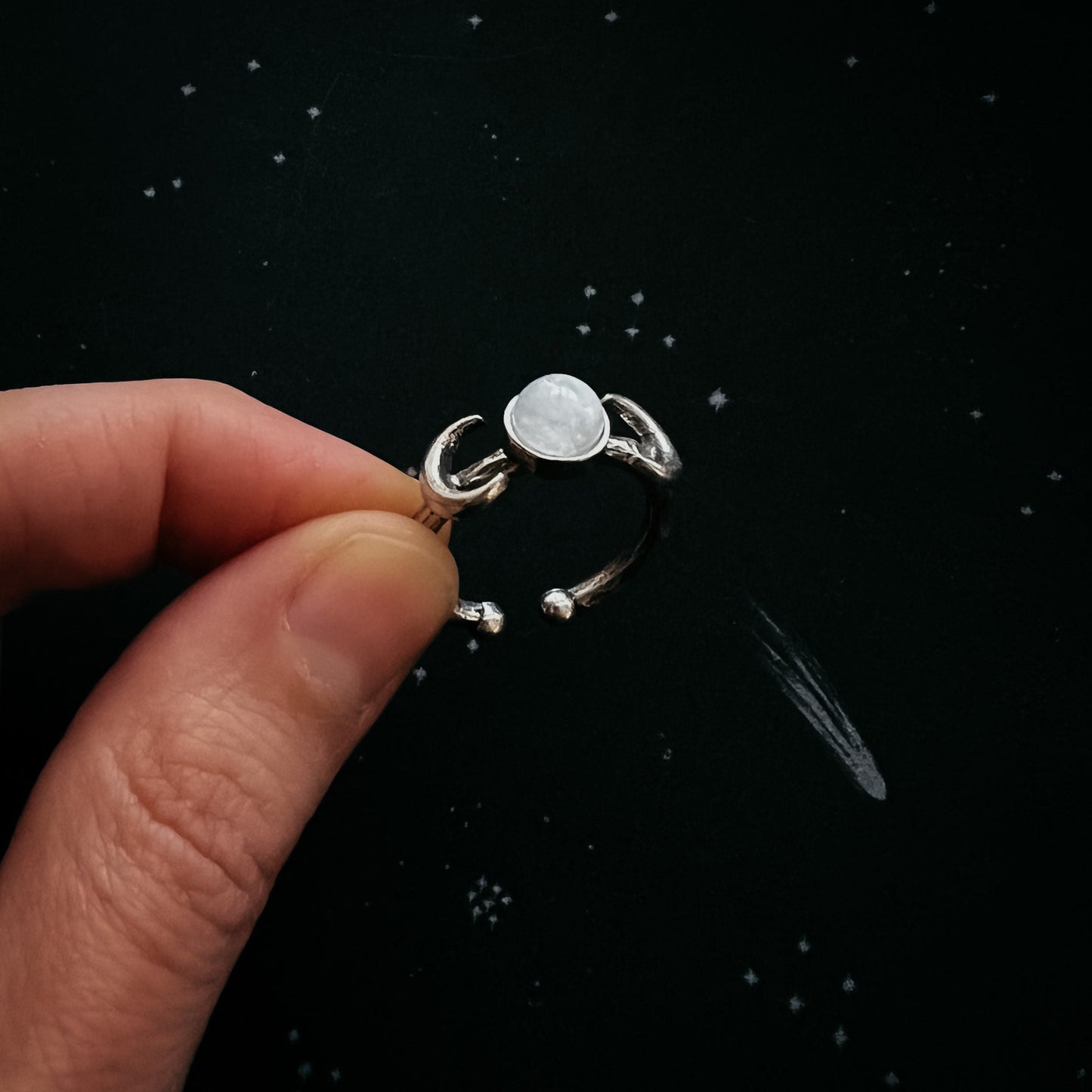 Silver ring with a central stone held by a hand against a black background