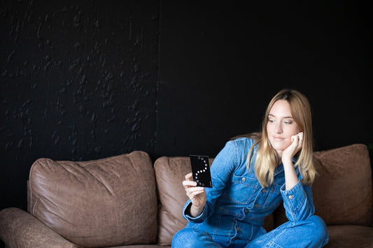 Woman in blue denim outfit sitting on a brown couch holding a smartphone with a dark background