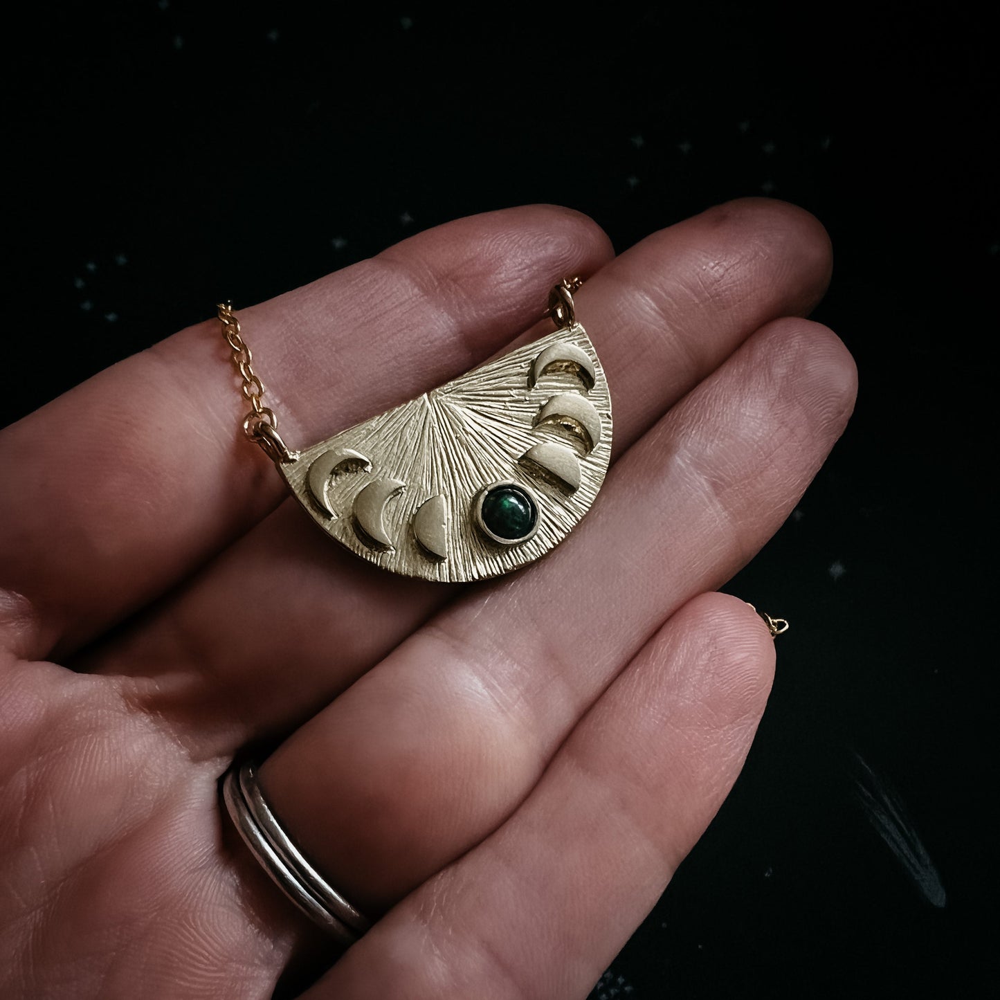 Gold necklace with a black opal gemstone pendant held in a hand against a dark background
