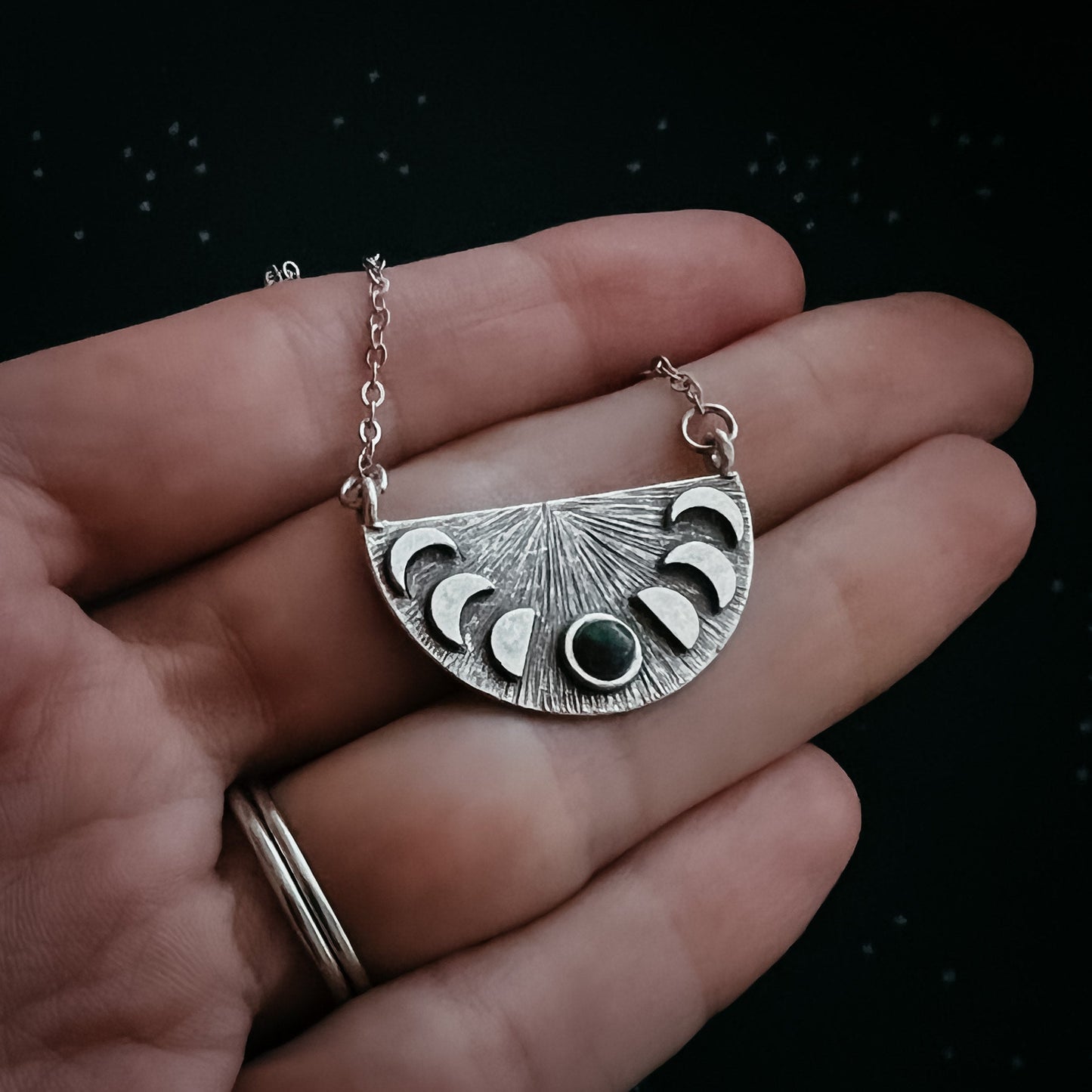 Silver necklace with a moon phase pendant held in a hand against a dark background