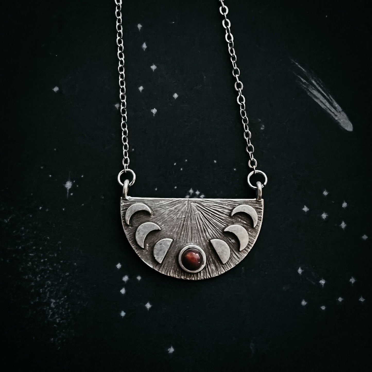 Silver necklace with a half-circle pendant featuring moon phases on a dark background